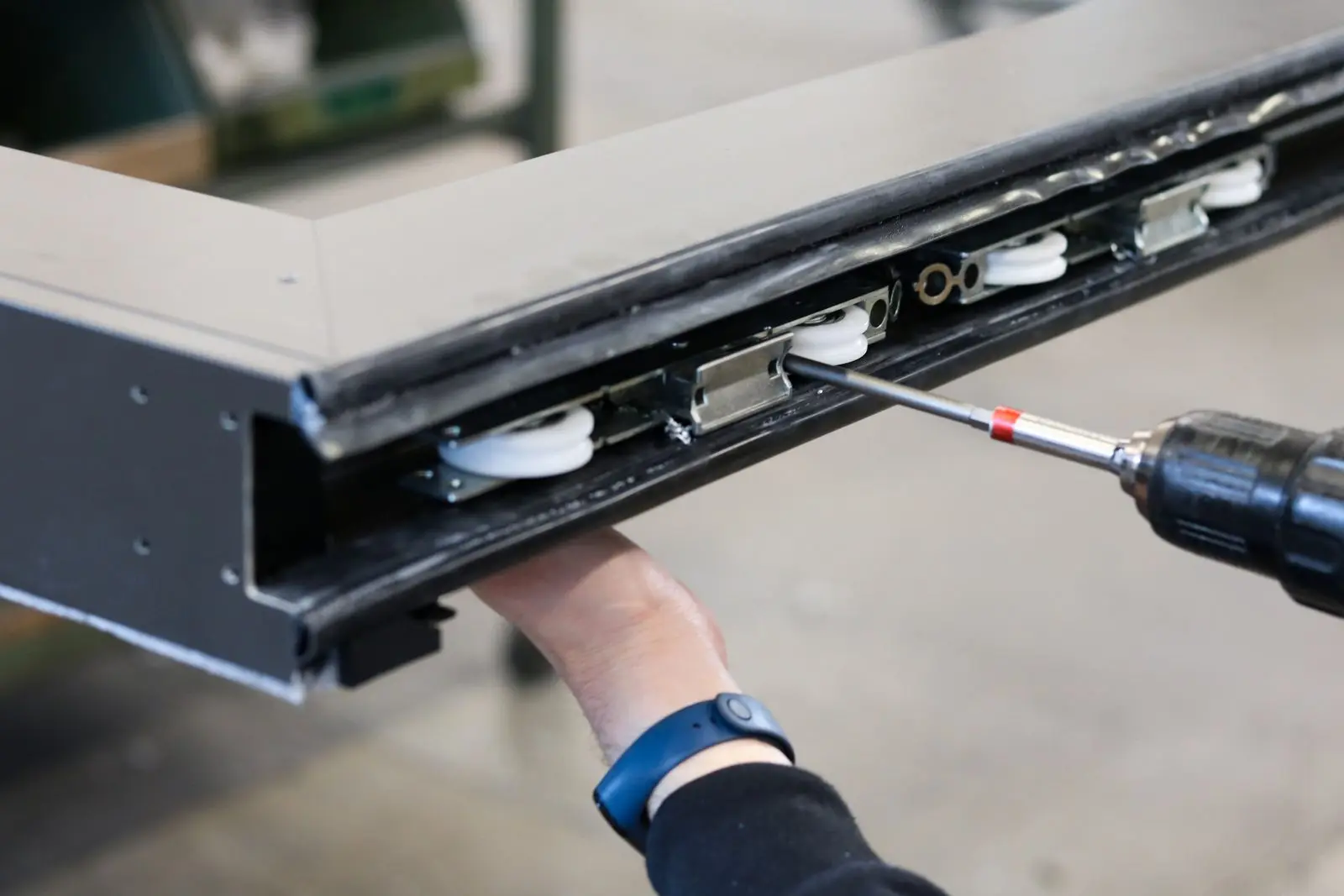 A cordless drill adjusting the rollers in the bottom rail of a sliding panel