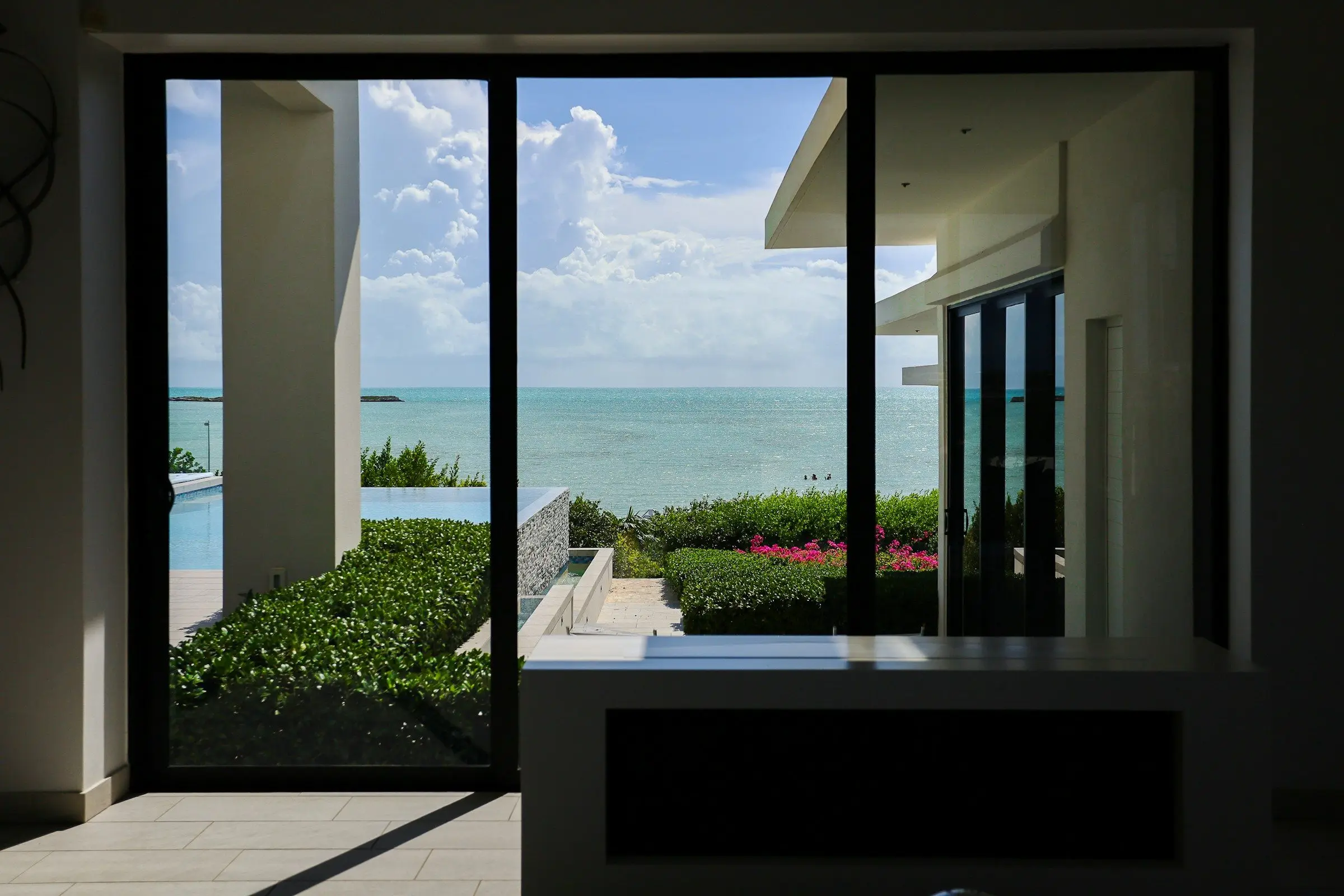 A large dark-framed sliding glass door looking out to a pool and the ocean