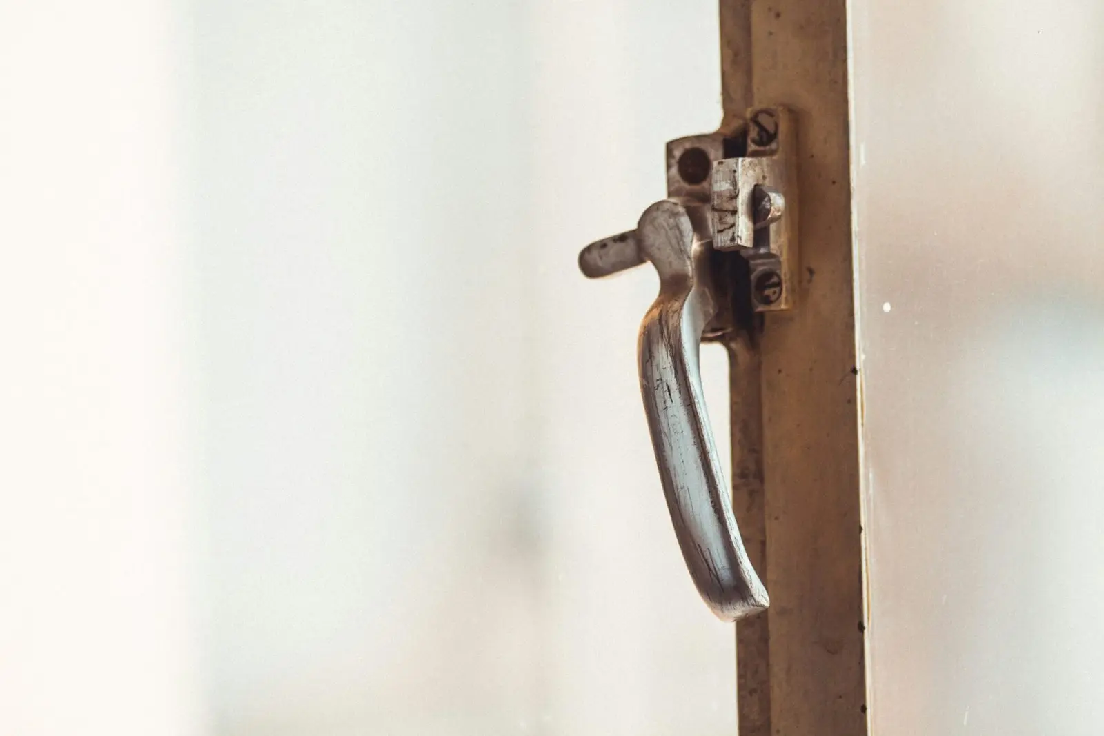 A worn metal window latch on a painted frame